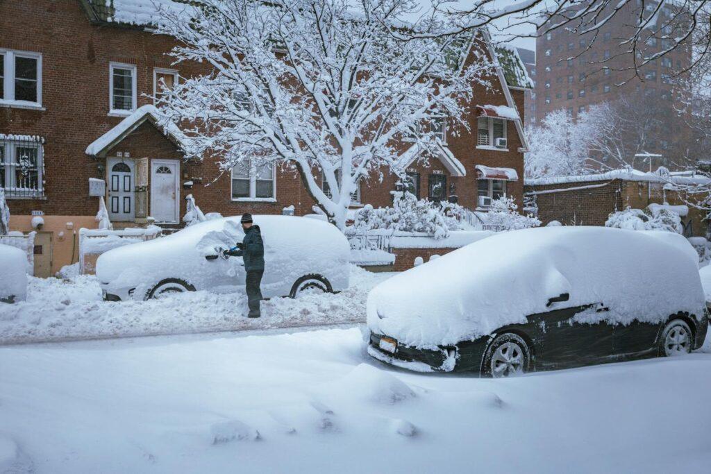 A person brushes snow off a car in a residential New York City neighborhood after a snowstorm.