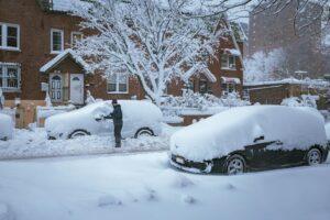 A person brushes snow off a car in a residential New York City neighborhood after a snowstorm.